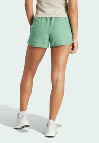 Pantalones cortos deportivos verdes con una cintura elástica, fabricados con un tejido ligero y con un dobladillo sencillo, combinados con calzado deportivo blanco.