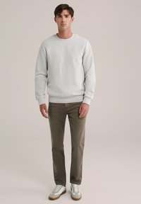 Pulover texturat gri deschis cu guler rotund, asociat cu pantaloni din bumbac subțiri de culoare verde măsliniu și adidași albi cu accente gri.