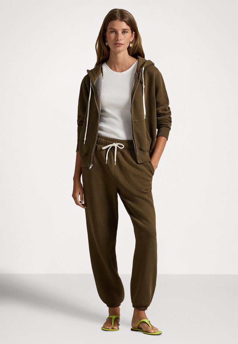 Brun zip-up hoodie med dragsko, vit ribbad tröja, matchande bruna sweatpants och gröna flip-flops. Mjukt tyg, avslappnad passform.