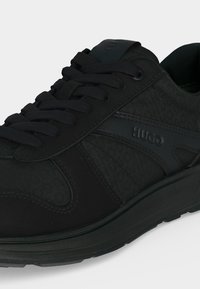 Μαύρο χαμηλό sneaker με υφασμένους και λείους πίνακες, μαύρα κορδόνια και ανάγλυφο "HUGO" στο πλάι.