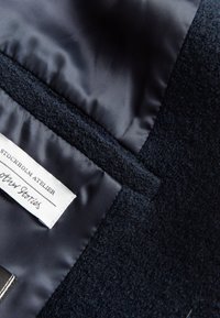 Marineblaues Wollmischgewebe mit glattem Satinfutter. Verfügt über ein Etikett mit "Stockholm Atelier" und eine vertikale Naht entlang der Kante.