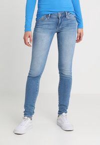 Vaqueros skinny de denim azul claro con un acabado deslavado, cinco bolsillos, presillas para el cinturón y un cierre estándar de botón y cremallera. Combinados con zapatillas blancas.