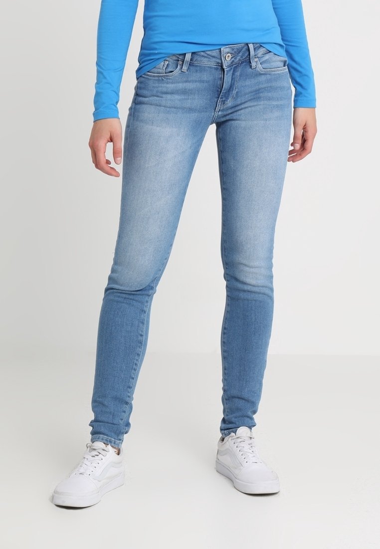 Vaqueros skinny de denim azul claro con un acabado deslavado, cinco bolsillos, presillas para el cinturón y un cierre estándar de botón y cremallera. Combinados con zapatillas blancas.