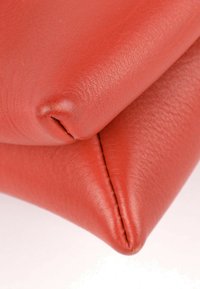 Gros plan d'un matériau en cuir rouge montrant une texture détaillée et des coutures pliées sur un fond clair.