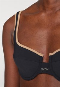 Μαύρο σουτιέν με μπεζ λεπτομέρειες. Διαθέτει έτοιμα cups, ρυθμιζόμενους ιμάντες και λογότυπο στο κέντρο μπροστά. Μαλακή υφή.