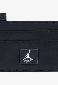 Schwarze Stofftasche mit horizontalen Nähten und einem rechteckigen schwarzen Etikett, das ein weißes Silhouetten-Logo und den Text "Flight" zeigt. Glatte Textur.