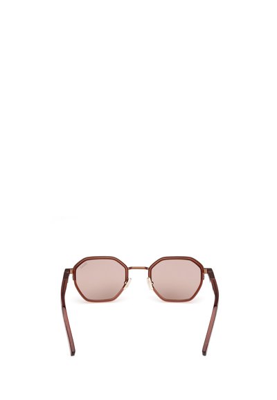 Ochelari de soare octagonali cu lentile de culoare maro, un pod subțire din metal și brațe din acetat maro ușor curbate. Prezintă accente subtile din argint.