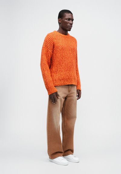 Sweater tricotat portocaliu cu o textură în voal, asociat cu pantaloni largi bej deschis și adidași albi. Design simplu și casual.