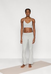 Ανοιχτό γκρι αθλητικό σουτιέν με ραμμένη μπροστινή πλευρά και λεπτές τιράντες, σε συνδυασμό με αντίστοιχο φαρδύ παντελόνι, και τα δύο κατασκευασμένα από απαλό, ελαστικό υλικό.