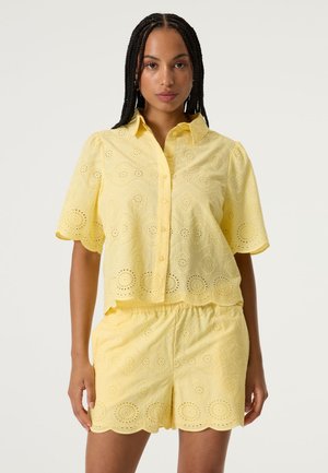Haut court jaune et short assorti en coton brodé, présentant des motifs découpés, des bords festonnés et des manches courtes.