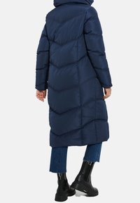 Marineblauwe, lange pufferjas met een geometrisch quiltpatroon, een capuchon en zijzakken. Gepaard met blauwe broek en zwarte stevige laarzen.