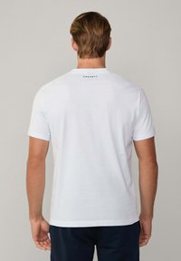 Camiseta de algodón blanca con cuello redondo, mangas cortas y un pequeño logo de "Hackett" impreso en la parte trasera, cerca del cuello.