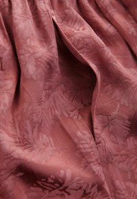 Tessuto strutturato in un colore rosa polveroso con un sottile motivo floreale. Il materiale appare morbido con una leggera luminosità e un drappeggio rilassato.