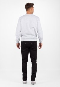 Grijze katoenen sweatshirt met ronde hals, gedragen met zwarte jeans en witte sneakers, gezien van achteren. Glad oppervlak, eenvoudig ontwerp.
