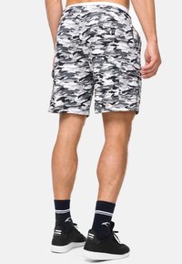 Shorts cargo gris et blanc en camouflage avec des poches latérales, une coupe décontractée et un tissu doux, associés à des baskets noires et des chaussettes rayées bleues.