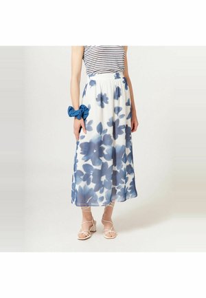 Frau trägt einen weißen Midirock mit blauen Blumenmustern, ein gestreiftes ärmelloses Oberteil, ein blaues Haargummi und weiße, mit Riemchen versehene Blockabsatz-Sandalen.