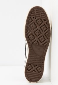 Brązowa gumowa podeszwa trampka z wytłoczonym geometrycznym wzorem oraz brandingiem "Converse All Star". Białe ścianki boczne z czarnym wzorem z kanwy.