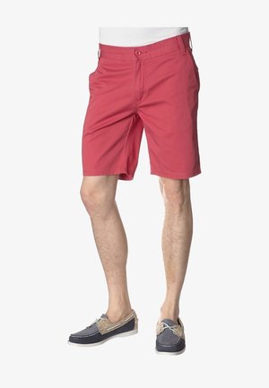 Helle rote Baumwollshorts mit Seitentaschen, Knopfverschluss und geradem Schnitt. Kombiniert mit marineblauen Bootsschuhen mit hellbraunen Akzenten.