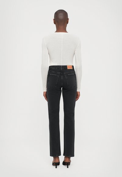 Black denim jeans with straight legs and rear pockets, paired with a fitted white long-sleeve top. Features a contrasting orange label.