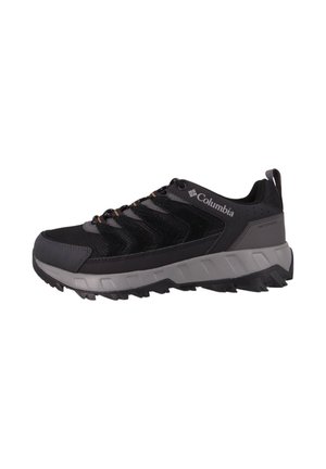 Zapatilla de senderismo negra con parte superior de malla y ante, suela de goma gris, acabado texturizado y acentos naranjas en los cordones y la marca. Presenta una asa en la parte posterior.
