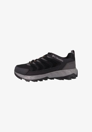 Zapatilla de senderismo negra con parte superior de malla y ante, suela de goma gris, acabado texturizado y acentos naranjas en los cordones y la marca. Presenta una asa en la parte posterior.