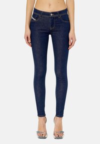 Jeans oscuros ajustados de mezclilla con cinco bolsillos, costuras en contraste y cierre de botón en el frente. Acentuados con un sutil logo en el bolsillo.