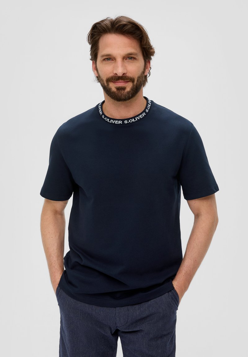 Granatowa koszulka z krótkim rękawem wykonana z miękkiego materiału, z okrągłym dekoltem i czarno-białymi detalami brandingowymi.