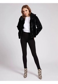 Chaqueta de piel sintética negra con capucha, combinada con una camiseta blanca y leggings negros. Completada con botas de tacón alto con estampado de serpiente.