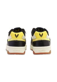 Svarta och gula sneakers med vita och bruna accenter, featuring en texturerad häl, gummisula och en framträdande logotyp på baksidan.