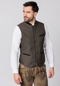 Dunkles, gemustertes Weste mit strukturierter Oberfläche, ausgestattet mit einem hohen Kragen, dekorativen Knöpfen und schrägen Taschen, kombiniert mit hellen Ärmeln.