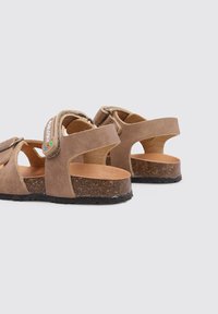 Sandalias de ante marrón con diseño abierto, correas ajustables, plantilla de corcho y suela de goma. Presenta un acento colorido en la correa.
