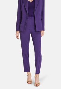 Purple tailored suit with structured blazer and slim-fit pants, made from smooth fabric. Accented with gold heeled sandals.