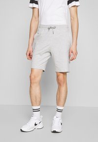 Shorts en mélange de coton gris avec taille élastique, cordon de serrage, deux poches latérales et une coupe ajustée, associés à des baskets blanches et des chaussettes rayées.