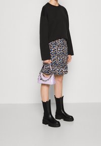 Maglietta nera a maniche lunghe, gonna a fiori con dettagli blu, borsa lavanda con tracolla a catena e stivali neri con tacco spesso.