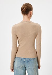 Top a maniche lunghe beige a coste con scollatura rotonda e forma aderente, abbinato a jeans a vita alta blu chiaro. Dettaglio in tessuto testurizzato.