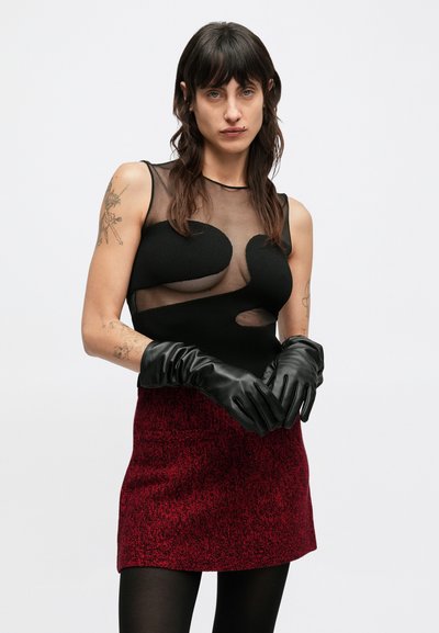 Czarna siateczkowa bluzka z zaokrąglonymi wycięciami, zestawiona z głęboko czerwonym, teksturowanym mini spódnicą oraz czarnymi skórzanymi rękawiczkami o gładkim wykończeniu.