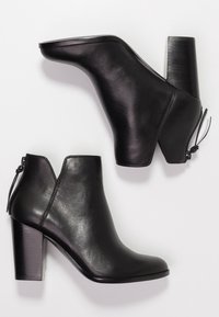 Botas de cuero negras hasta el tobillo con punta redonda, tacón alto en bloque, cremallera lateral y un acabado ligeramente texturizado.