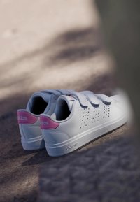 Zapatillas blancas con acentos rosas, con parte superior de cuero liso, correas con cierre de gancho y bucle, detalles perforados y suela de goma.