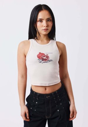 Joven con cabello largo y negro lleva un top corto blanco con gráfico de granada y pantalones negros de cintura alta.