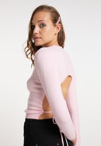 Maglione lavorato a maglia rosa chiaro con maniche lunghe, design con schiena aperta e lacci regolabili. Tessuto morbido con dettagli a coste sul bordo.