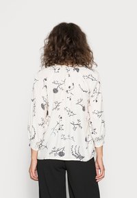 Witte blouse met zwart bloemenpatroon, lange mouwen met elastische boorden, geplooide achterkant en lichtgewicht stof.