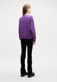 Felpa viola oversize con polsini e orlo a costine, abbinata a pantaloni neri aderenti e stivali chunky neri con plateau.