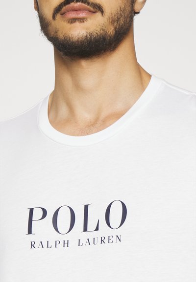 Biele bavlnené tričko s okrúhlym výstrihom a výrazným nápisom "POLO RALPH LAUREN" v námorníckej modrej farbe na prednej strane.