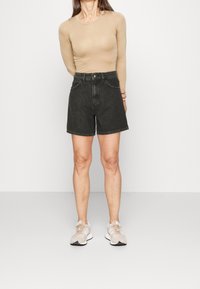 Svarta denimshorts med hög midja och vida ben, med framfickor och rak fåll. Kombineras med en beige långärmad topp och neutrala sneakers.