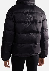 Personne portant une doudoune noire brillante vue de dos, avec des poignets élastiques et un motif matelassé horizontal.