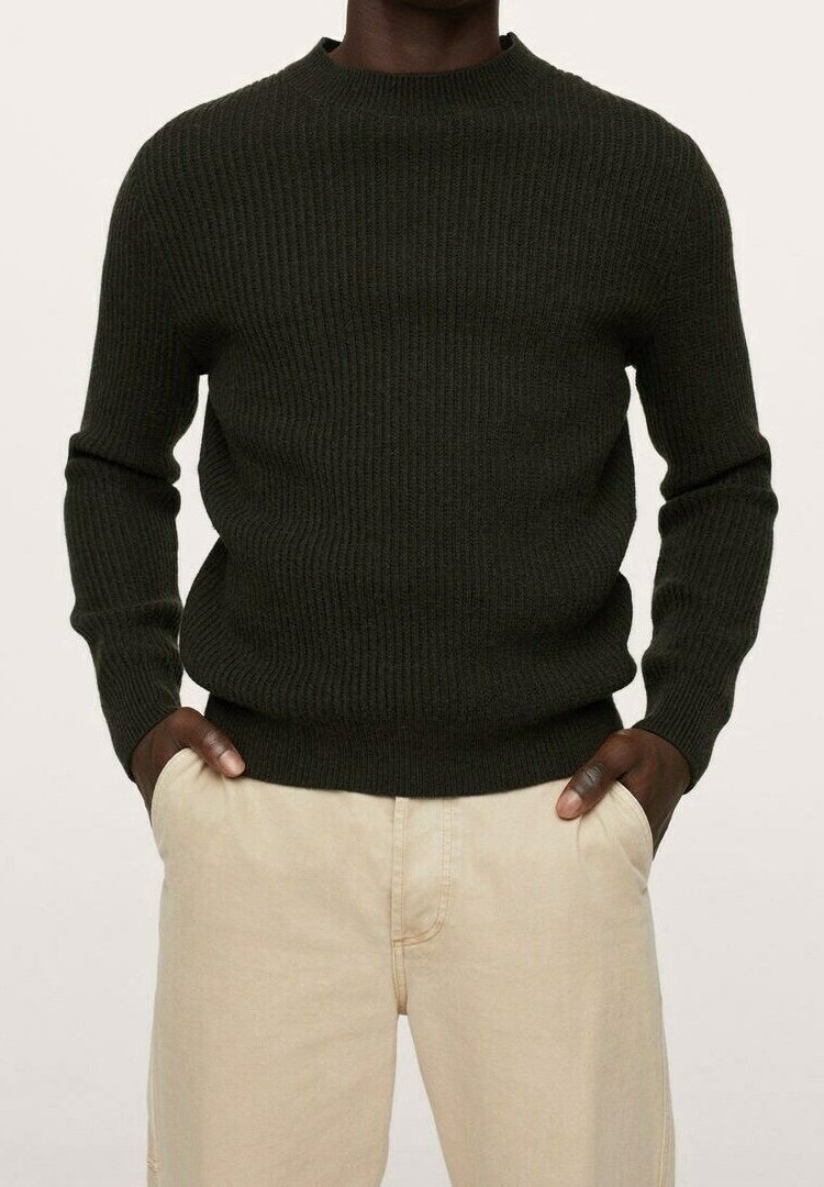 Donkergroene ribgebreide trui met een ronde hals en lange mouwen, gecombineerd met lichtgekleurde broek. Geappliqueerde afwerking.