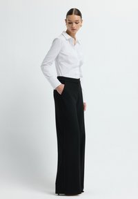 Witte blouse met lange mouwen en kraag, met een knoopsluiting aan de voorkant, gecombineerd met zwart, hooggewaisted, wijde broek met zijzakken.