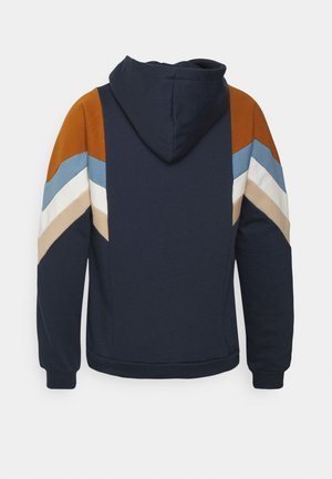 Sweat à capuche bleu marine avec des bandes en chevrons orange rouille, bleu clair, blanc et beige sur les manches et le haut du dos.
