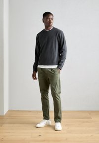Hanorac lung gri închis cu guler alb, asortat cu pantaloni subțiri verzi deschis și adidași albi cu accente bej.