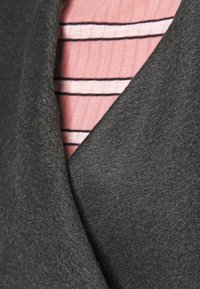 Ciemnoszara, teksturowana tkanina o miękkiej, filcowej powierzchni, nałożona na różowy element odzieży z cienkimi poziomymi paskami.